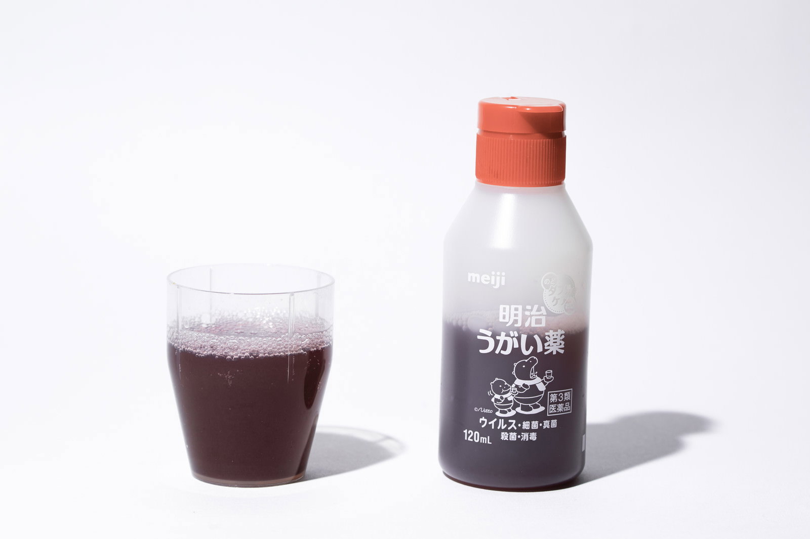 白い背景に置かれた赤いキャップのうがい薬ボトルと茶色い液体の入ったコップ