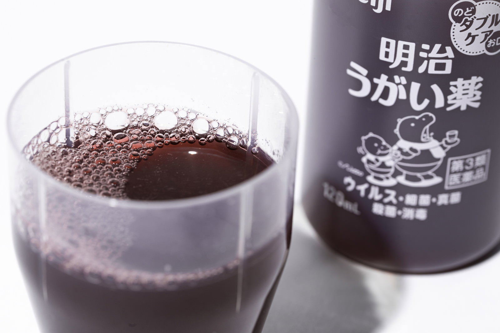 透明なコップに注がれた茶色いうがい薬とボトル容器