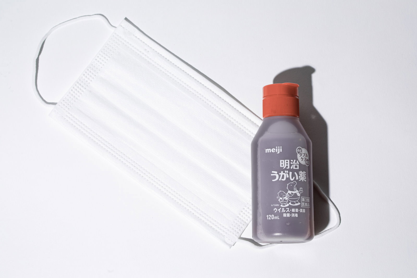 白い背景に置かれた茶色いボトルのうがい薬と白いマスク