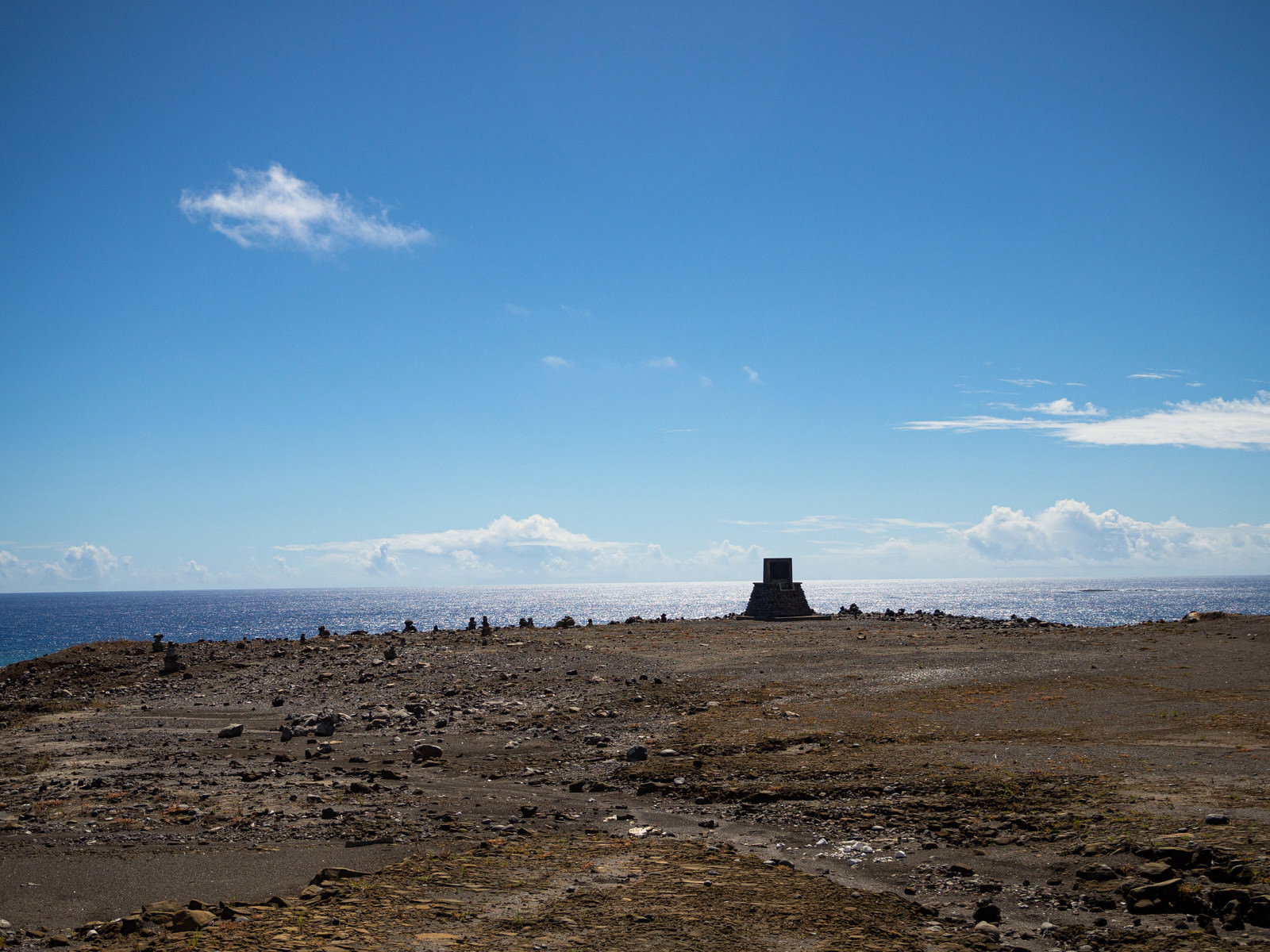 硫黄島の海岸に建つ西大佐の碑と周辺に積まれた石、青空と水平線