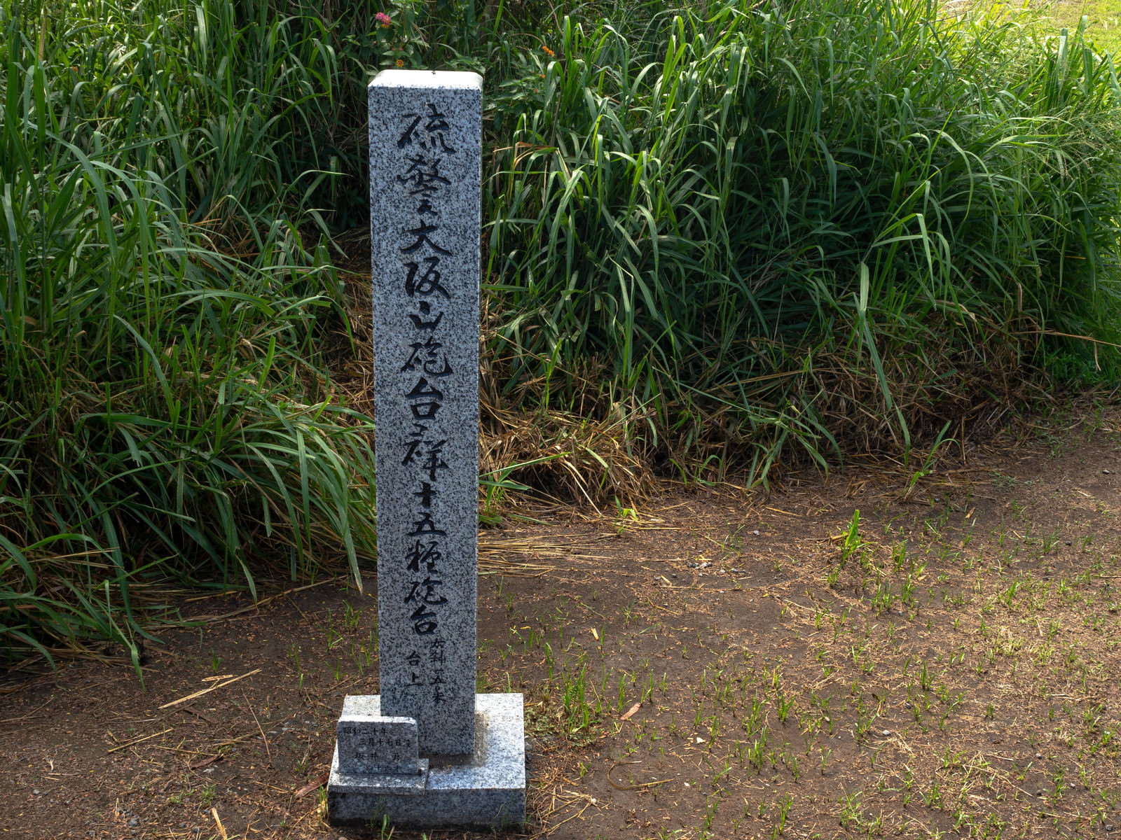 緑の草地に立つ大阪山砲台道標の石柱