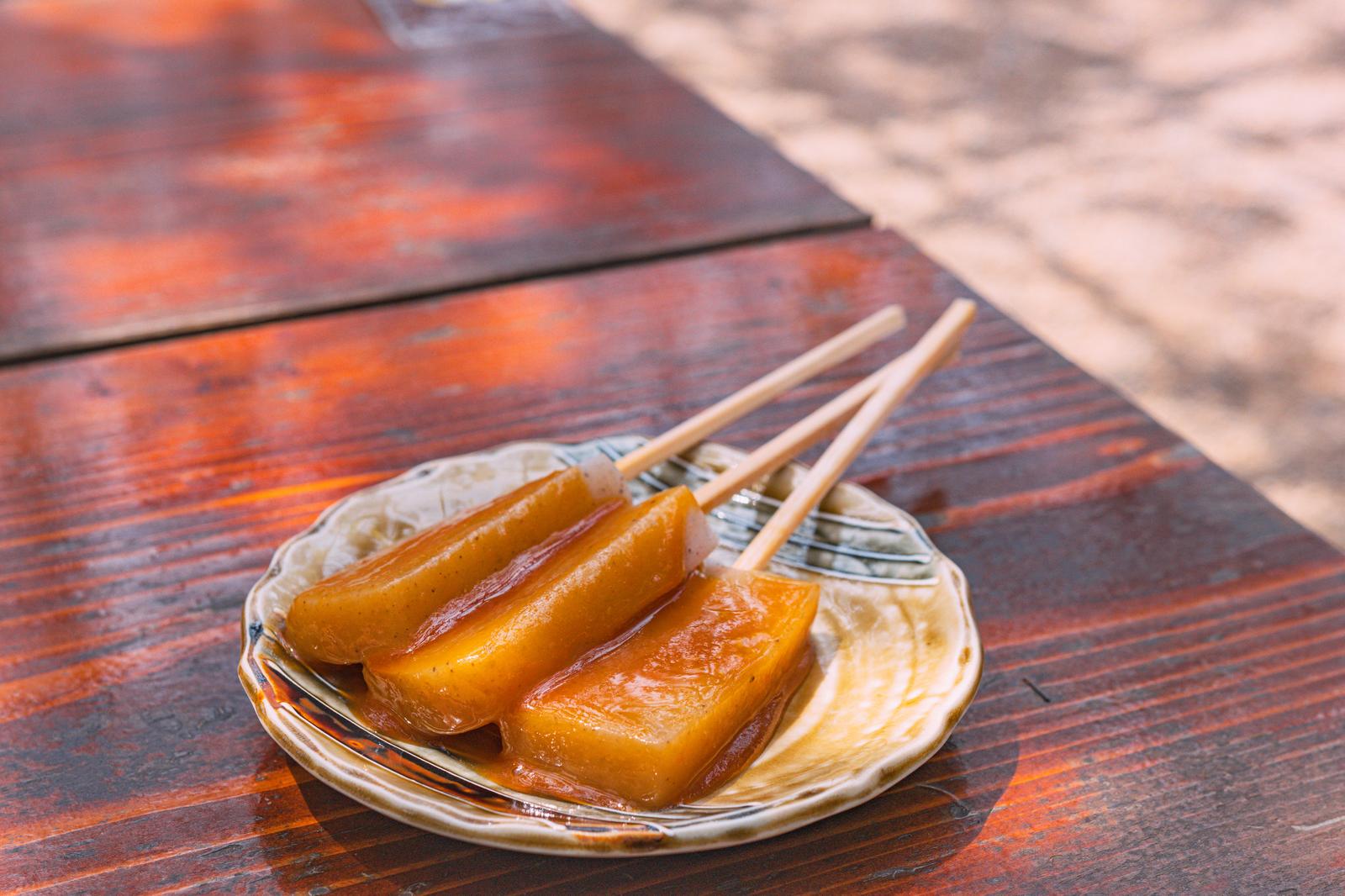 串に刺した蛇の鼻の味噌田楽がこんにゃくの串焼きとして木製テーブルの上に盛り付けられている