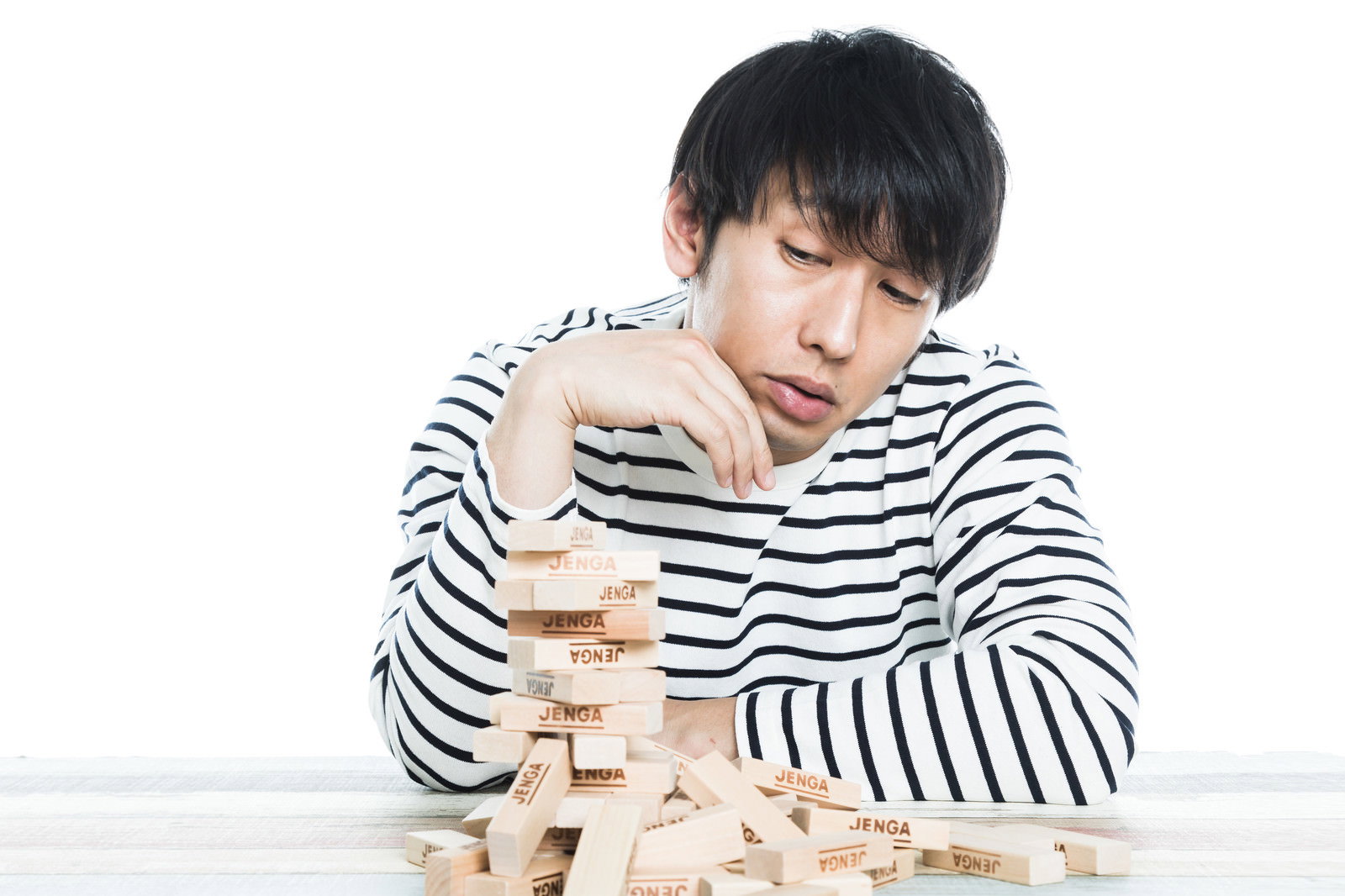 崩れたジェンガブロックを見つめるボーダーシャツの男性［モデル：大川竜弥］