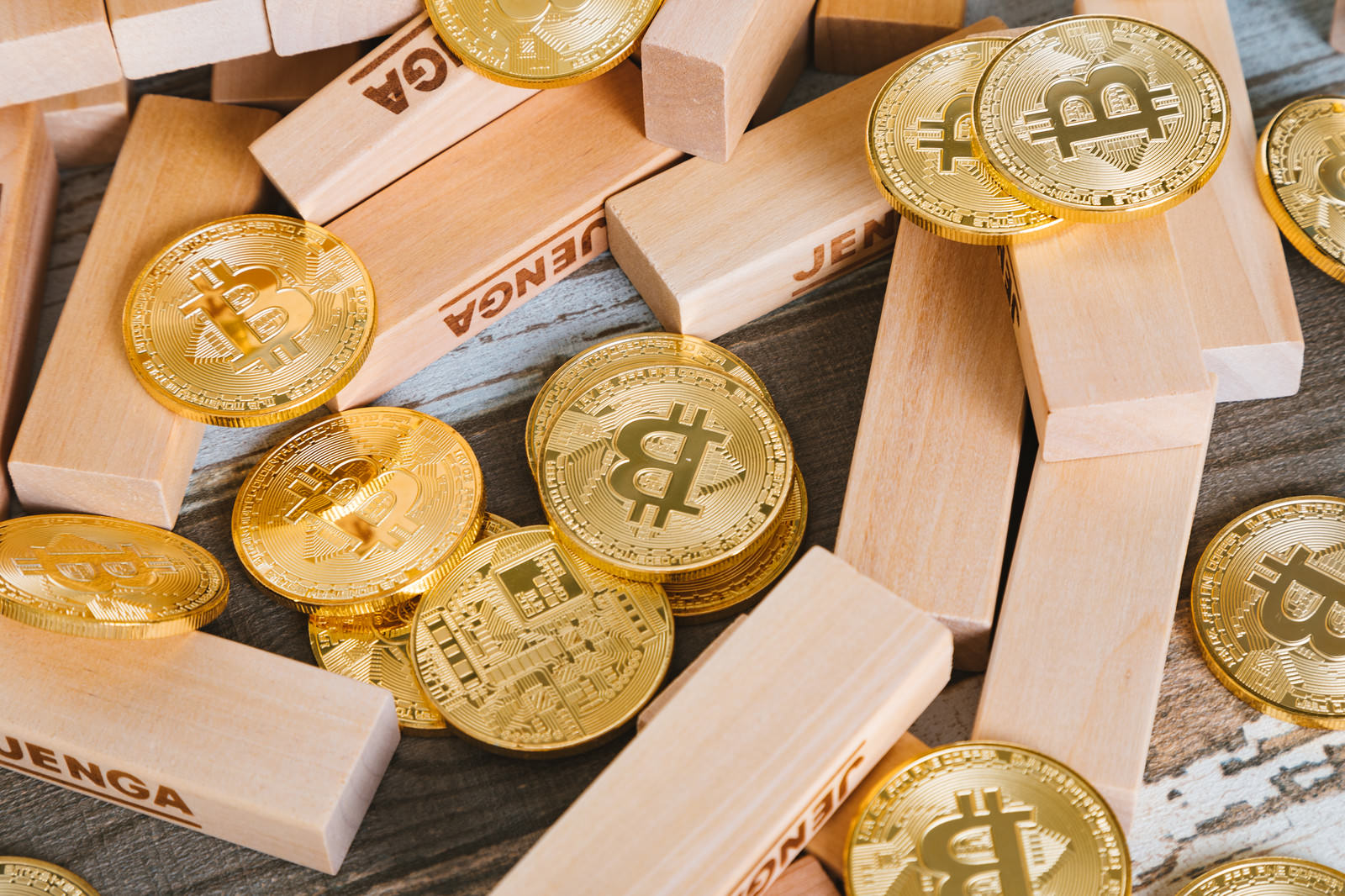 崩れたジェンガブロックの周囲に金色のビットコインコインが散らばっている様子