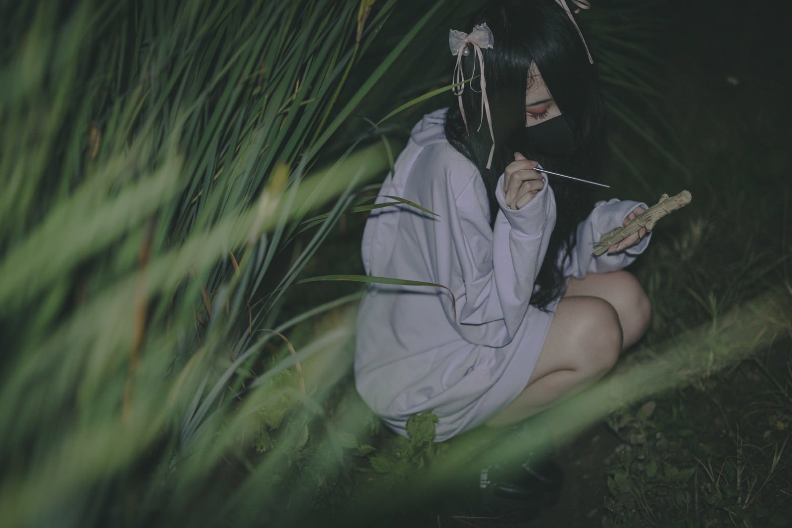 暗い草むらの中で藁人形に五寸釘を刺している地雷系女子［モデル：緋真煉］