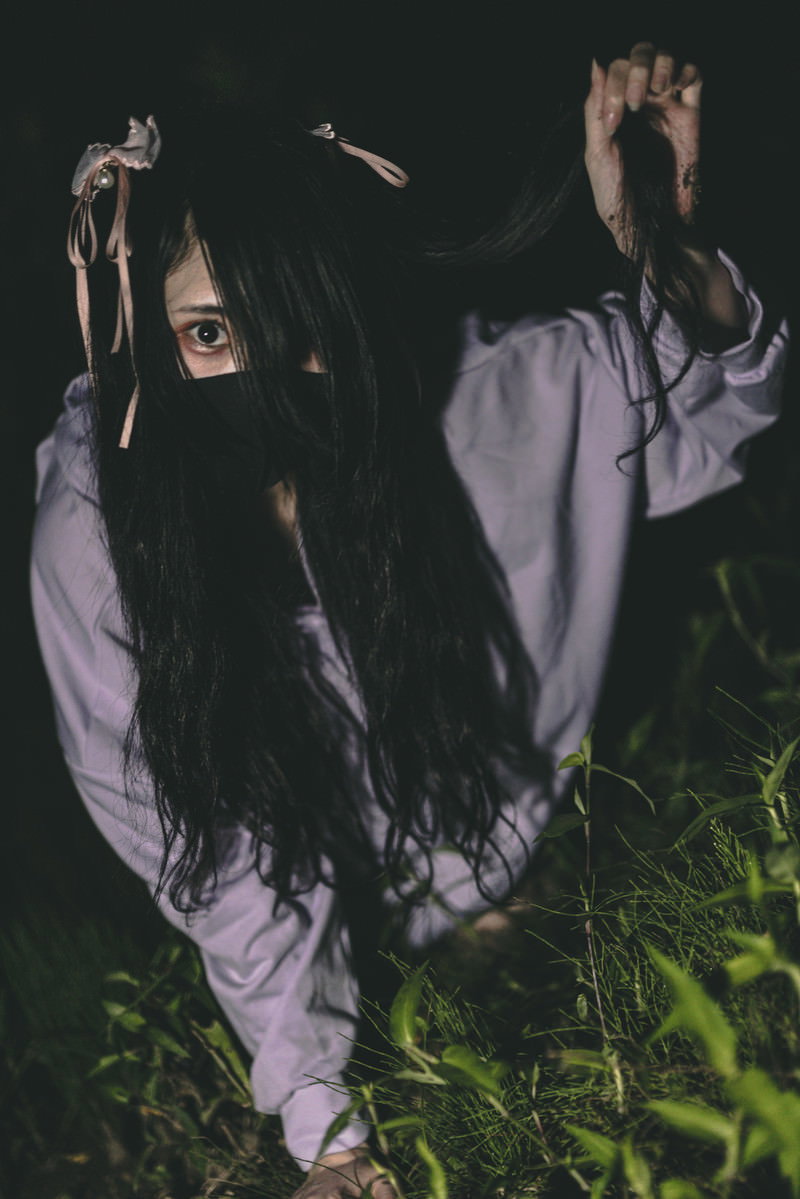 暗闇の中で紫色の服を着てマスクをした女性が地面を這いずり出てくる様子［モデル：緋真煉］