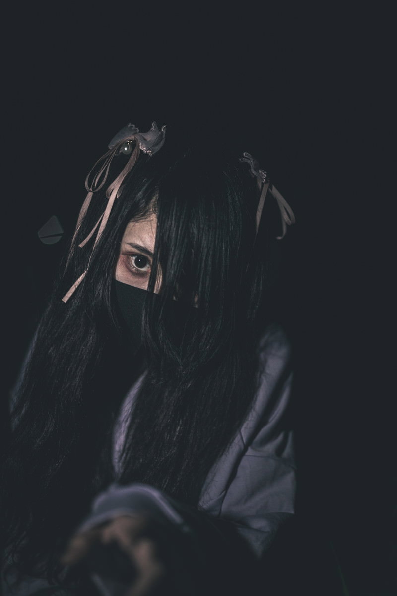 暗い背景で黒髪を手で覆い隠している地雷系女子［モデル：緋真煉］