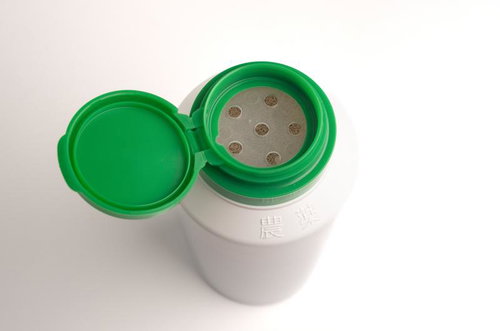 緑の蓋が開いた顆粒の除草剤の白い容器