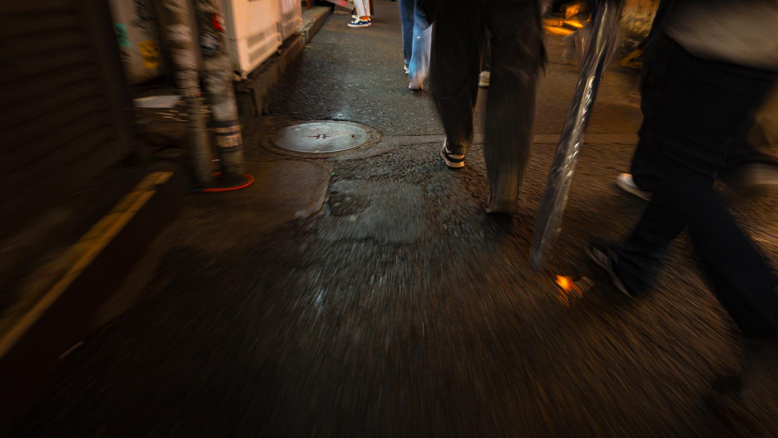 夜の裏道の濡れた路面を歩く人々の足元