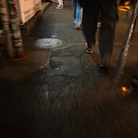 夜の繁華街の裏道を歩く複数人の足元の風景の写真