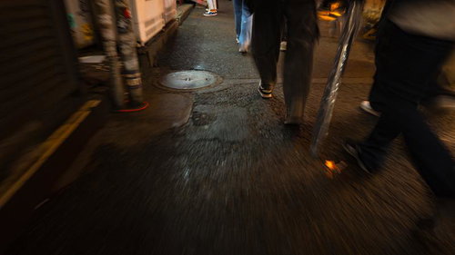 夜の繁華街の裏道を歩く複数人の足元の風景
