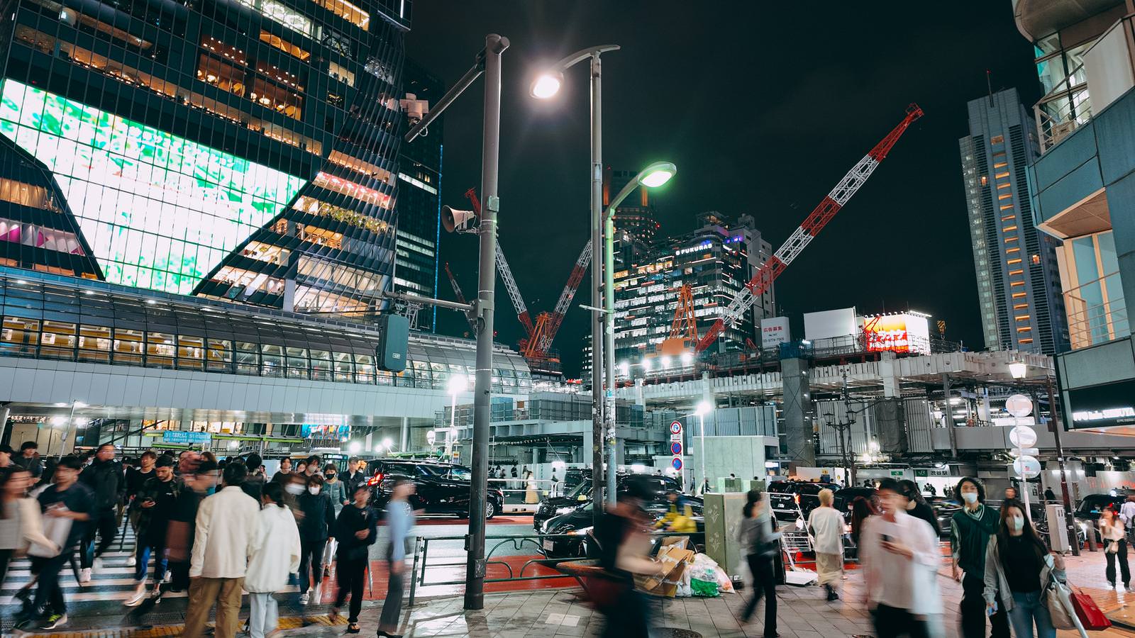 夜の宮益坂下交差点で多くの人が往来し、ビル群とクレーンが見える渋谷の夜景