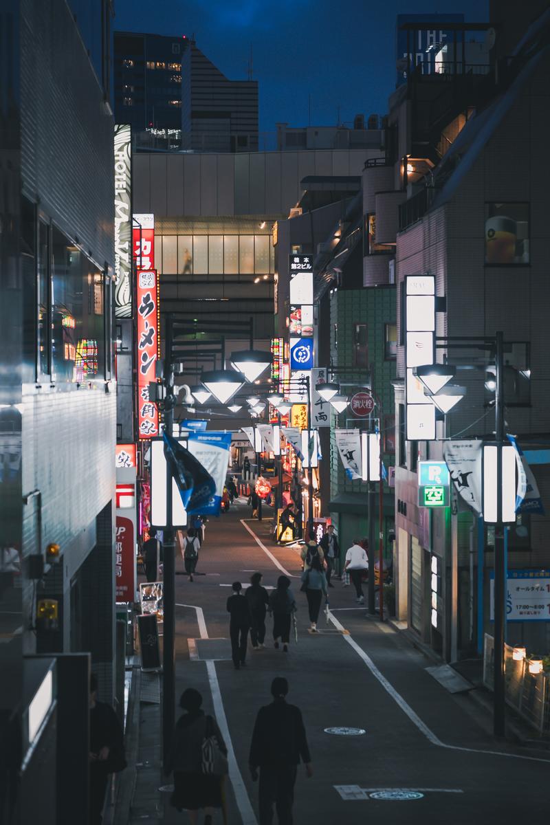夜間に人々が行き交う渋谷中央街の繁華街。ネオン看板と飲食店の灯りが路地を照らしている