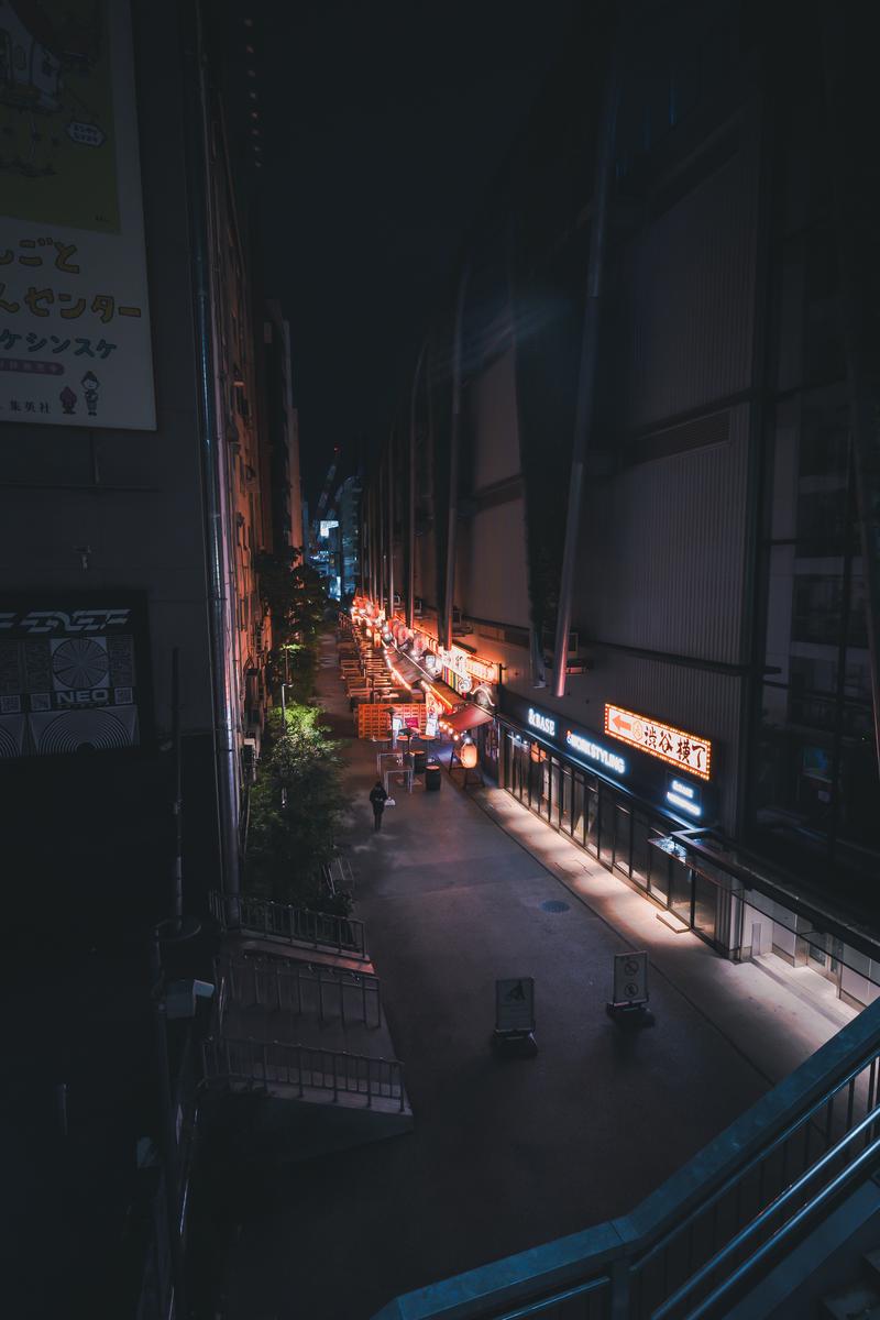 夜間に照明で照らされた渋谷横丁の路地。両側のビルに提灯と看板が灯っている