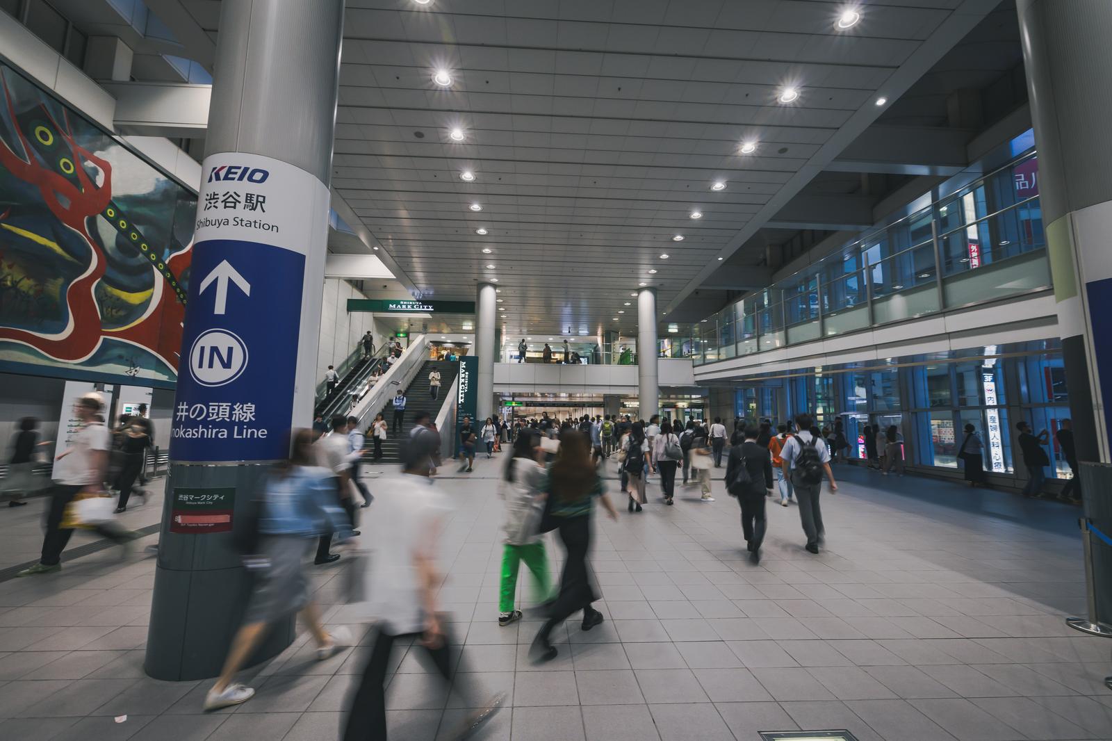 渋谷駅の広い自由通路を移動する多くの乗客たちと、KEIO渋谷駅の案内表示が立つ様子