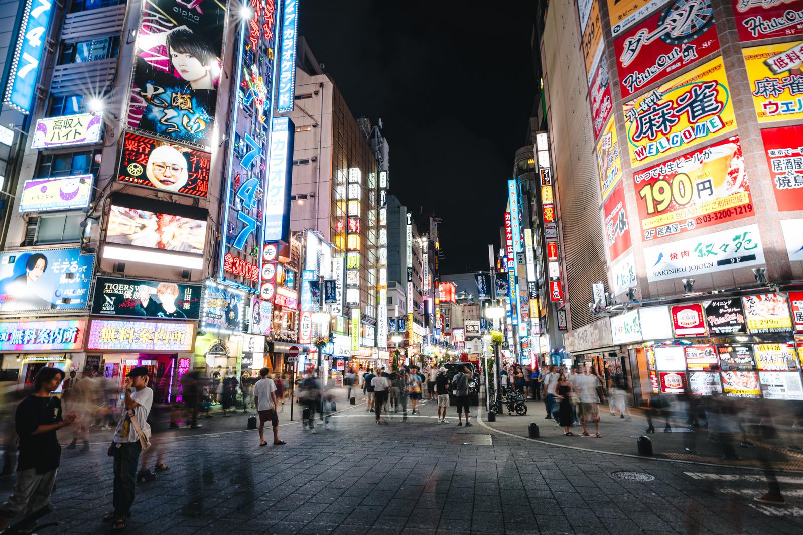 新宿セントラルロードの夜間の繁華街。ネオン看板が灯り、多くの人が行き交っている
