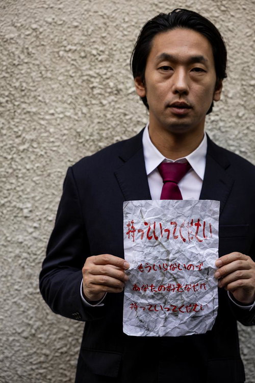 濃紺スーツの男性が赤い文字の怪文書を両手で掲げるポートレート