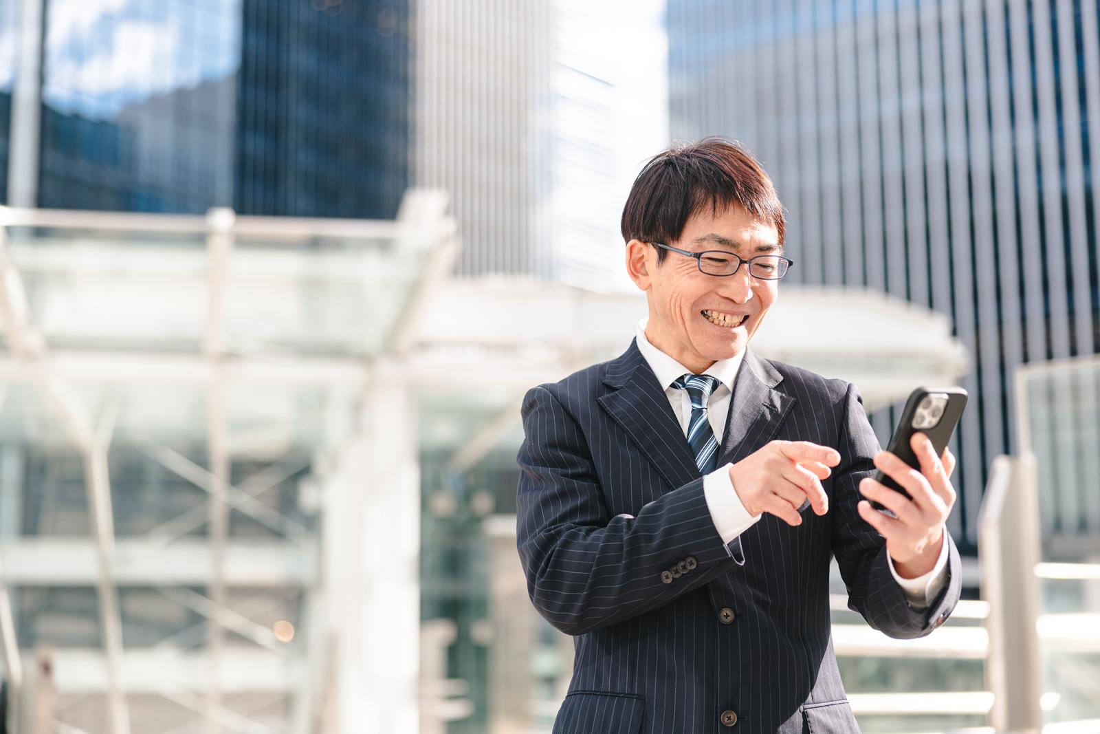 スマートフォンを見て笑顔で喜ぶスーツ姿の男性営業マン［モデル：ガーミー］