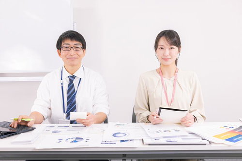 会議室で資料を見ながら打ち合わせする男性部長と女性社員