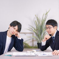 資料を前に考え込む2人のビジネスマンの打ち合わせ風景の写真