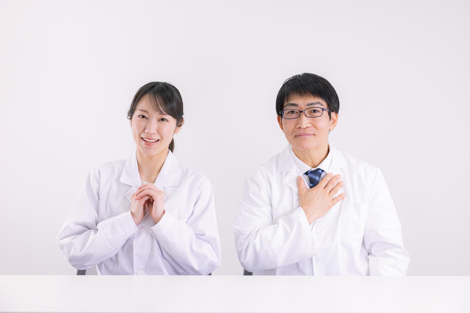 白衣姿の男女医師が笑顔で患者に安心感を与えている［モデル：ガーミー SAKI］