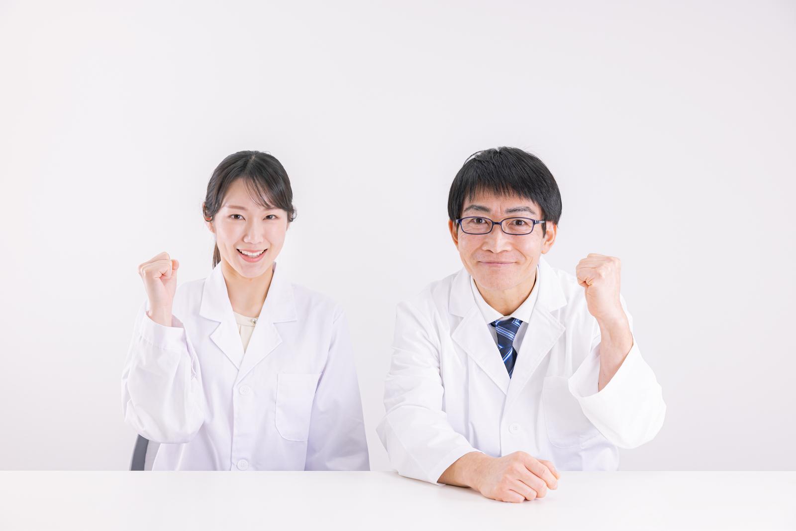 白衣姿の男性医師と女性医師が両こぶしを上げてガッツポーズをしている［モデル：ガーミー SAKI］