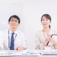 ホワイトボードを背に資料を見ながら会議に参加する男性と女性職員の写真