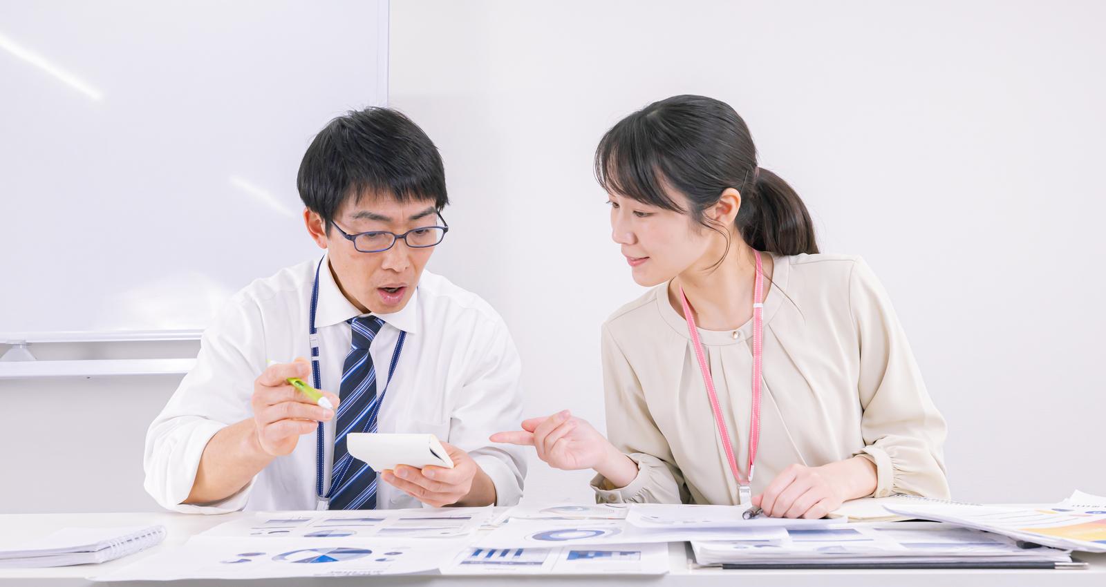 資料を見ながらディスカッションする男性と女性の職員［モデル：ガーミー SAKI］