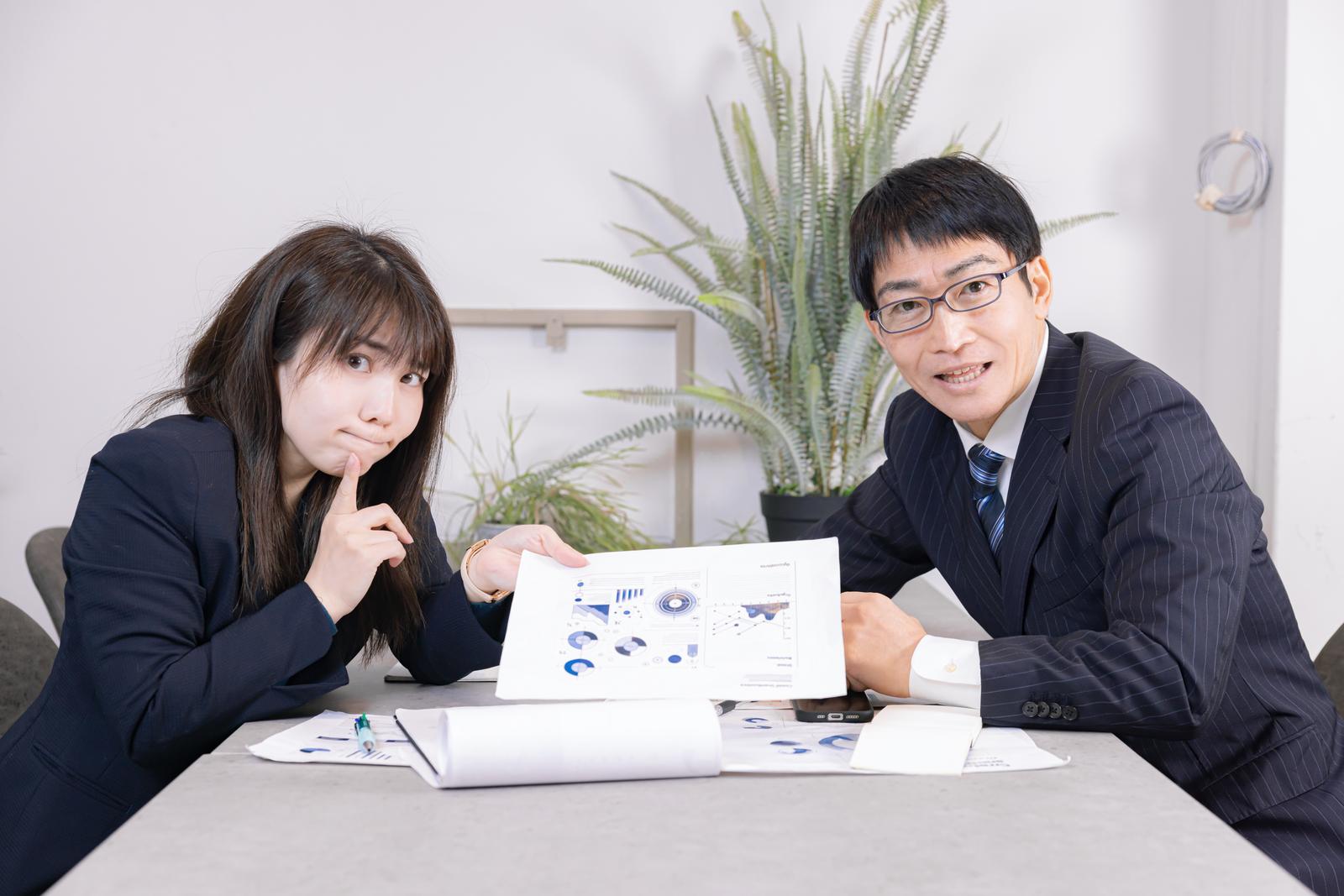 プレゼン資料を見せながら説明する男性と聞く女性社員［モデル：Lala ガーミー］