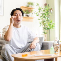 目がしょぼしょぼして目元を押さえる男性の写真
