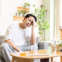 つらい頭痛で頭を抱える男性、ストレスや疲労による片頭痛の症状の写真