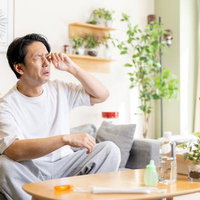 花粉症で目がかゆくつらい男性のリビングでの症状と対策の写真