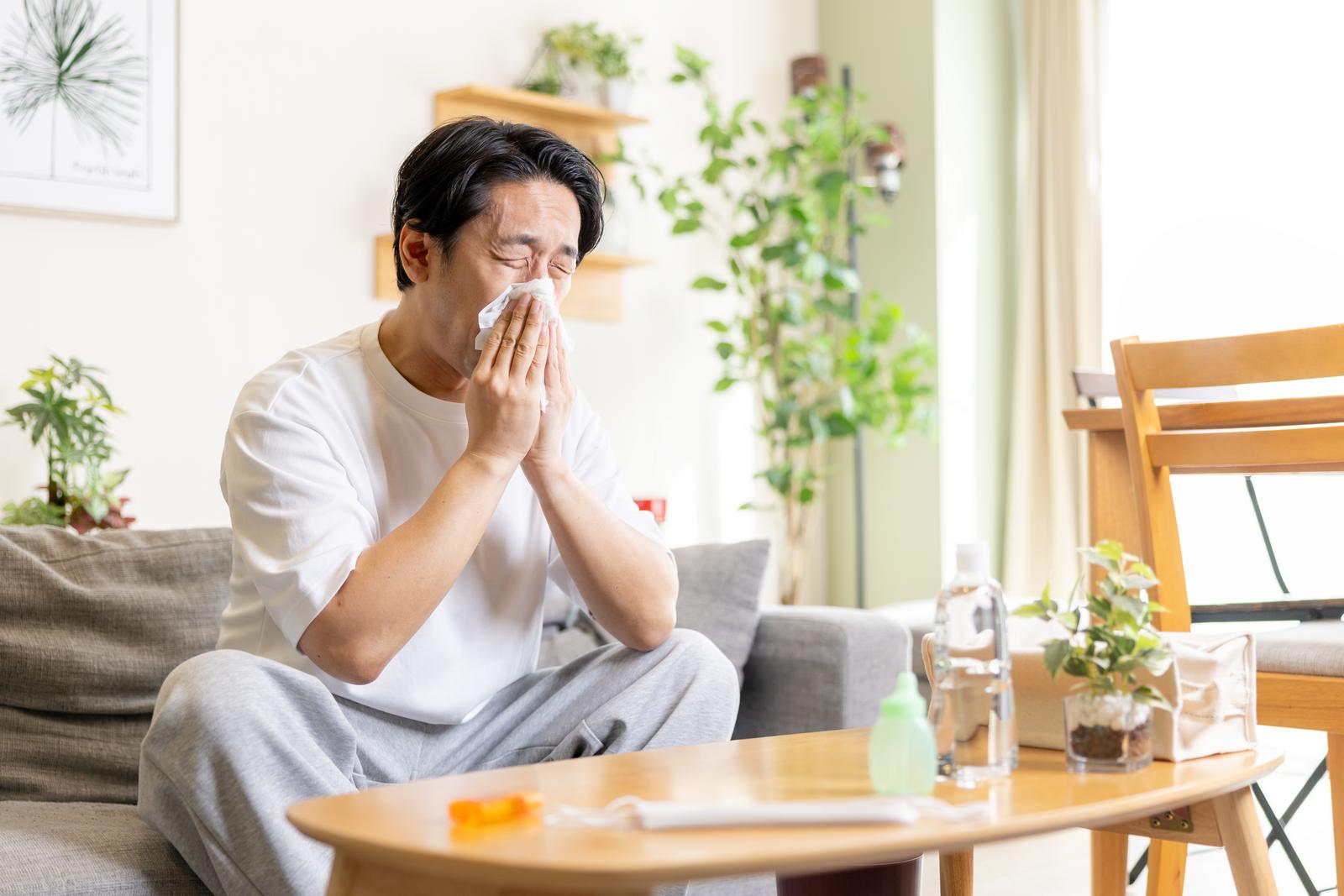 リビングでティッシュで鼻をかむアレルギー性鼻炎の男性［モデル：大川竜弥］