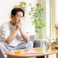 リビングでティッシュを使って鼻をかむアレルギー性鼻炎の男性の写真