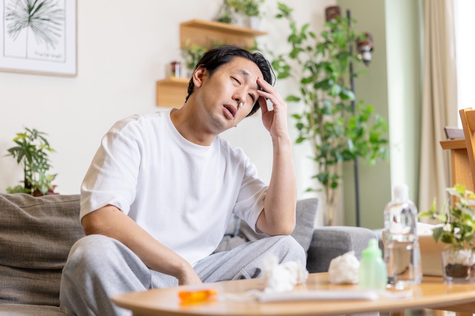 花粉症で頭痛により苦しそうな表情で顔に手を当てる男性［モデル：大川竜弥］