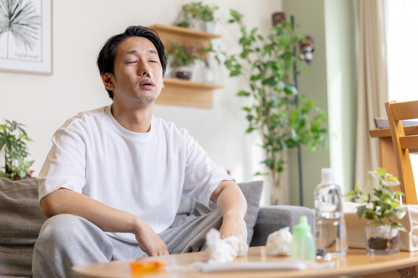 家でティッシュを手に目を閉じた男性［モデル：大川竜弥］