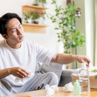 何度もティッシュで鼻をかむ花粉症の男性がテーブルで症状に苦しむの写真