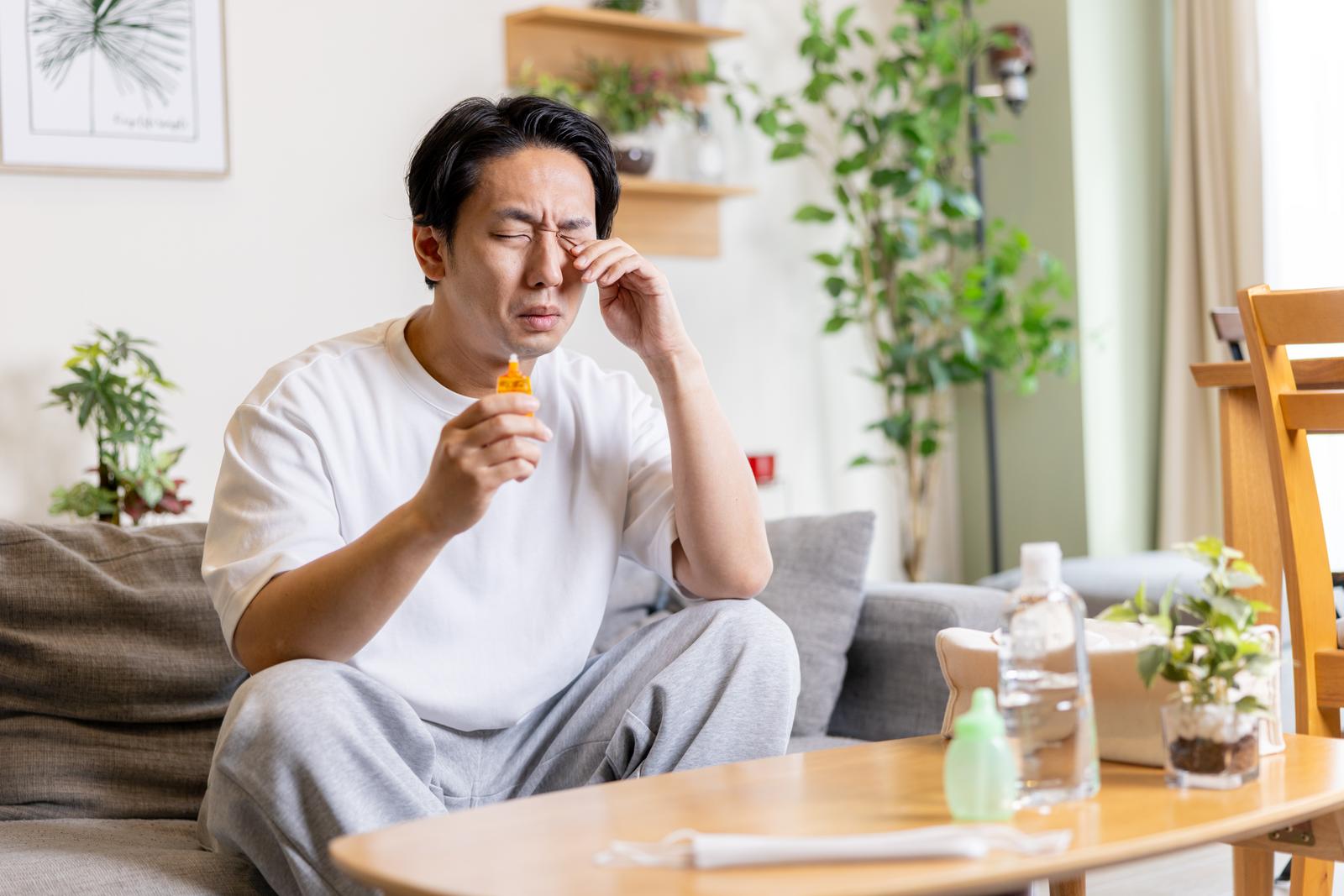 目のかゆみで目薬をさす男性。ソファーに座り、目を閉じて右目に点眼している［モデル：大川竜弥］