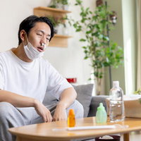 鼻にティッシュを詰めてうつむく男性、アレルギー症状の写真