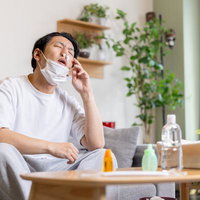 鼻栓とマスクの両方をしながら鼻をおさえる花粉症で苦しむ男性の写真