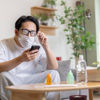 マスクをしながらメガネをかけると曇ってスマホが見えなくなる男性の写真