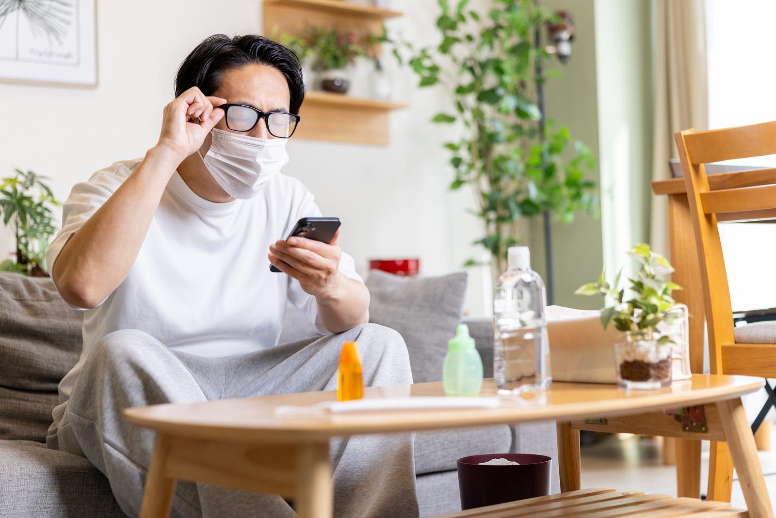 眼鏡が曇ったマスク姿の男性がスマートフォンを持っている［モデル：大川竜弥］