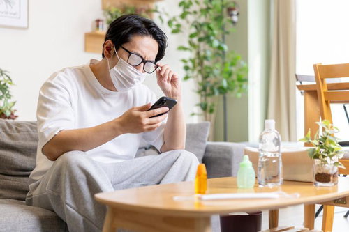 マスク着用時に眼鏡が曇ってしまう男性がスマートフォンを操作