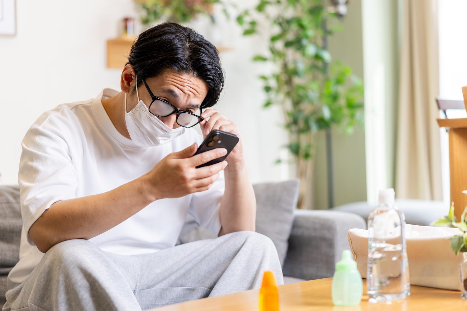 マスクをして眼鏡が曇り、スマホを見ながらイライラしている男性［モデル：大川竜弥］