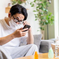 マスクをすると眼鏡が曇ってイライラしながらスマホを見る男性の写真