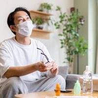 マスクをしながらメガネを拭く男性の花粉症対策の写真