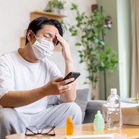 アレルギー性鼻炎がつらくて部屋の中でもマスクをつける男性の写真