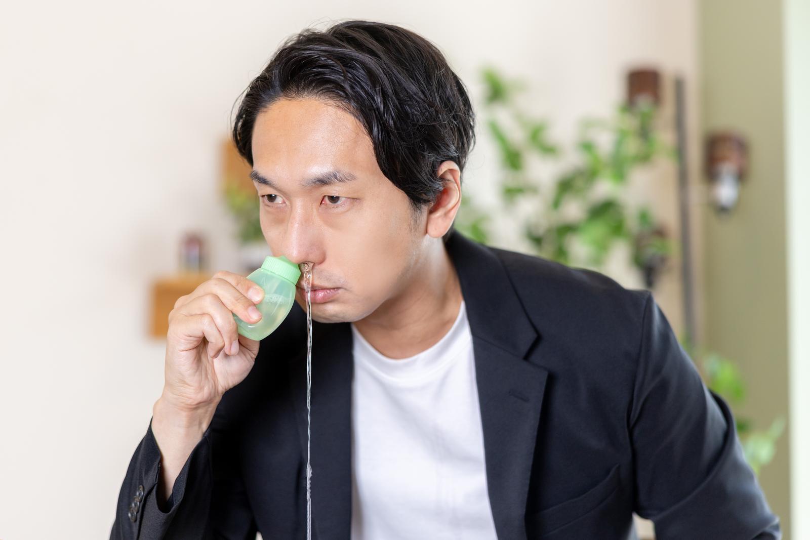 緑色の鼻洗浄器具を使用して鼻うがいをする男性［モデル：大川竜弥］