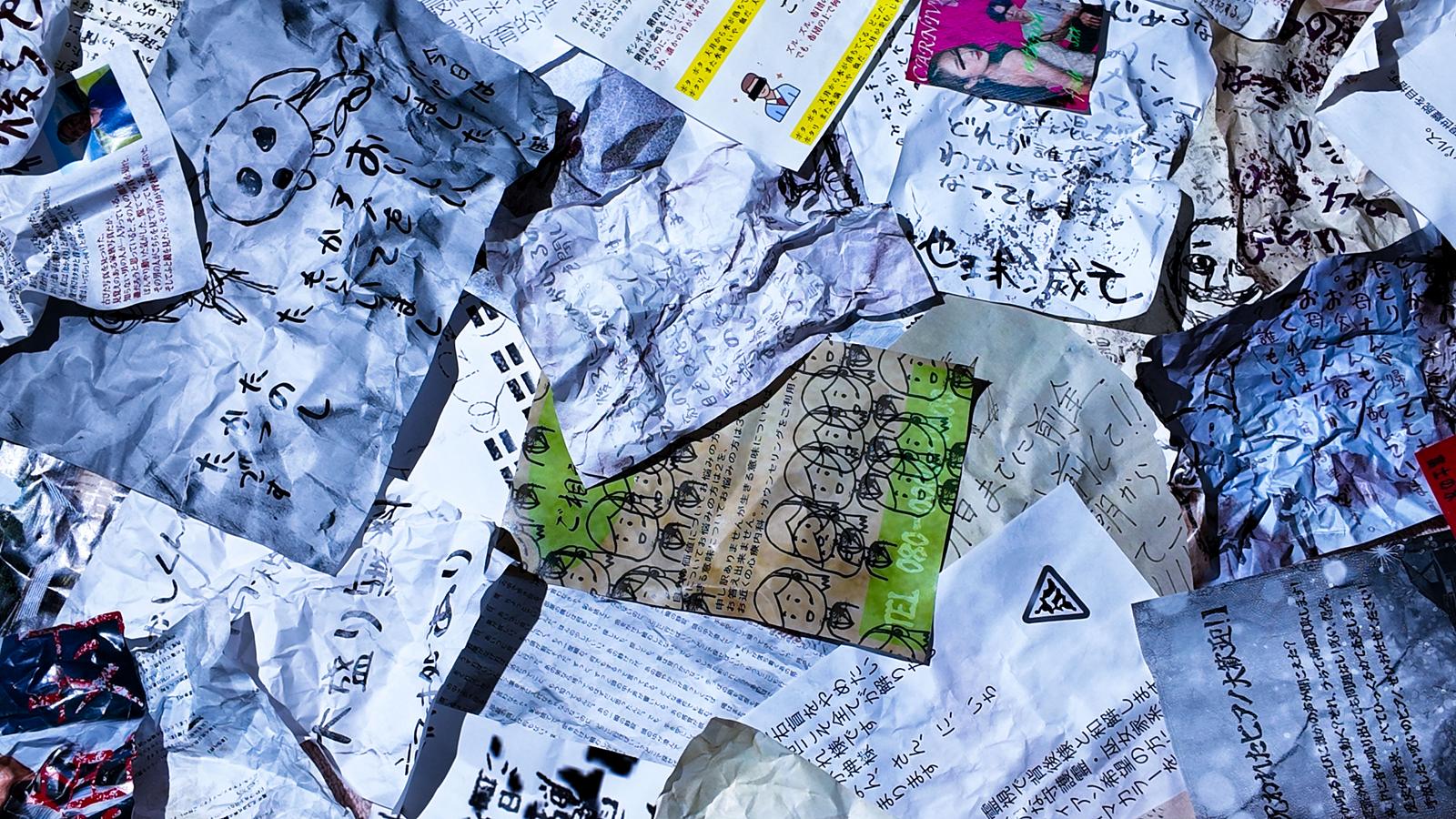 手書きの文字やイラストが描かれた怪文書と紙片が散乱している様子