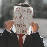 紙袋で顔を隠した黒スーツの男性が怪文書を掲げるポーズの写真